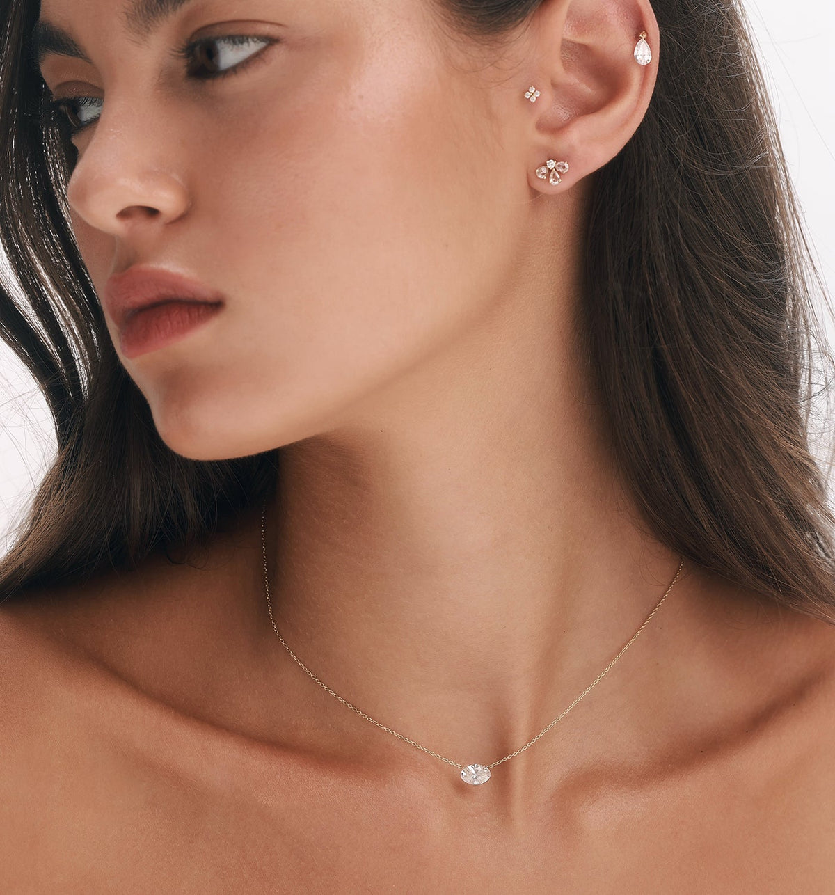 OVAL shape floating lab diamond necklace in yellow gold styled with GIA diamond earring, floating pear lab diamond helix earring and FOUR diamond tragus earring in curated ear composition on model